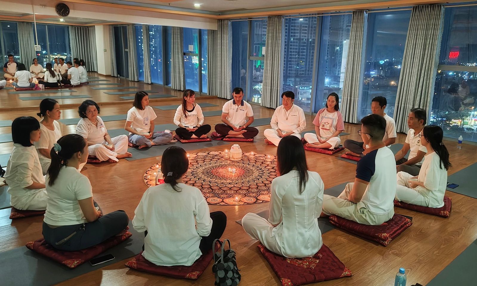 Lớp thiền Thiền Việt ngồi thành vòng tròn quanh nến, phía sau là cửa kính nhìn ra thành phố về đêm